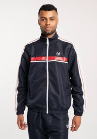 Giacca a track navy in tessuto liscio, con strisce orizzontali rosse e bianche, colletto alto, zip completa e polsini elasticizzati. Logo sul petto.