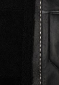 Black jacket featuring a side of textured shearling and smooth leather, with a silver zipper and a pronounced pocket detail.