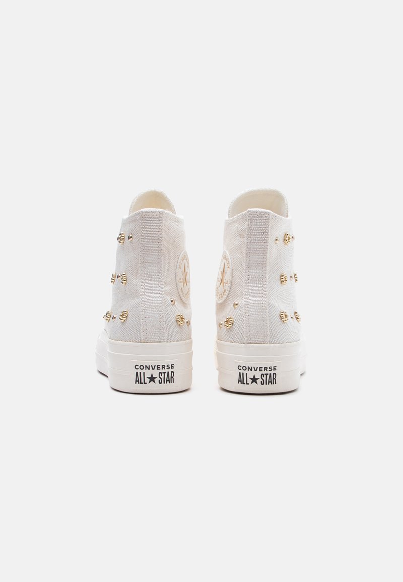 Sneakers Converse All Star bianche alte con borchie dorate sulla tela, viste da dietro su uno sfondo bianco uniforme.