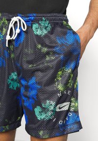 Shorts en mesh noirs avec un motif floral bleu et vert, taille élastique avec cordon blanc, et détail de logo au bas.