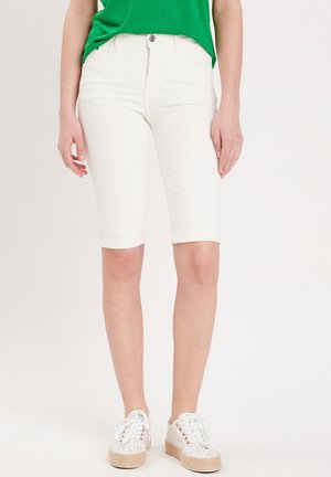 Shorts en denim blanc arrivee aux genoux avec un ourlet retroussé, associés à un t-shirt vert et des baskets à motifs. Style décontracté, coupe ajustée avec poches avant.