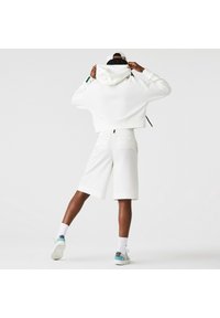 Sweat à capuche blanc court avec capuche et cordon de serrage, assorti à un short blanc jusqu'aux genoux. Comprend deux poches arrière, porté avec des chaussettes blanches et des baskets.