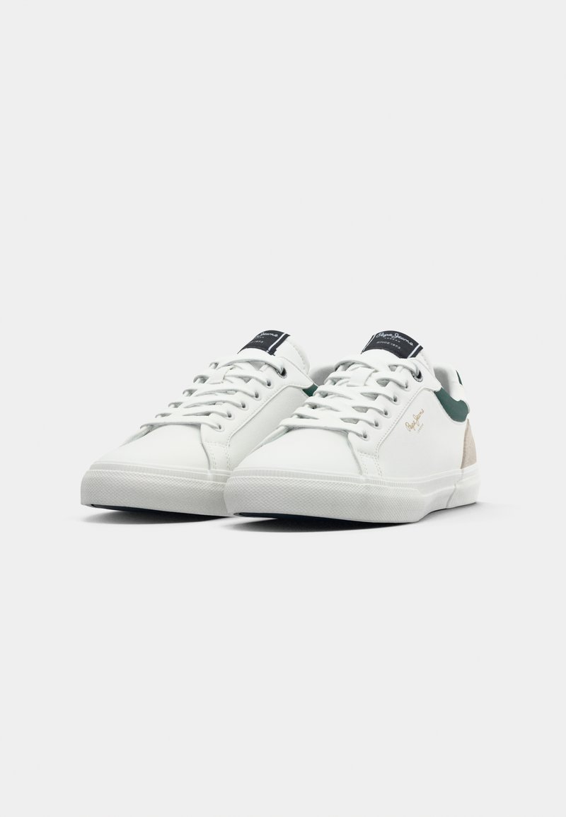Witte sneakers met een glad leren bovenwerk, groene accenten op de hak en een gegolfde rubberen zool. Uitrusting met witte veters en branding op de tong.