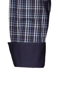 Polsino di una camicia a maniche lunghe a quadri blu e neri, realizzato in tessuto blu scuro e con una texture liscia, con orlo cucito.