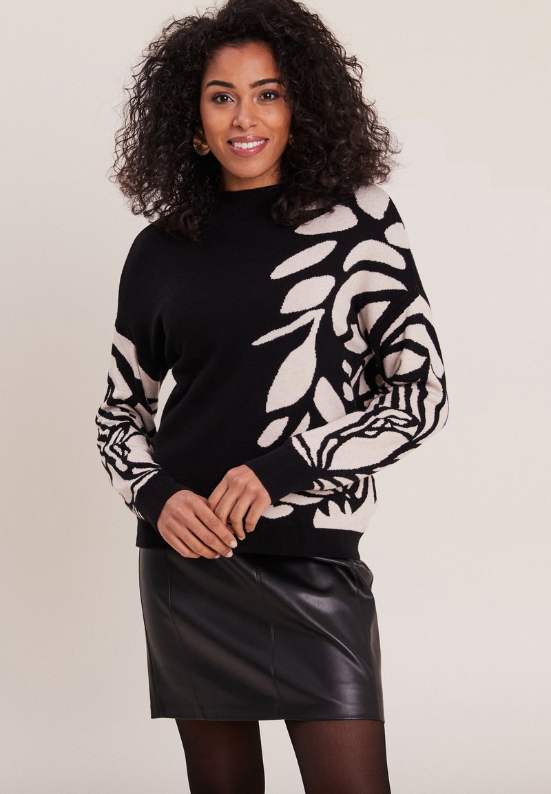 Schwarzer und cremefarbener Strickpullover mit botanischem Muster an den Ärmeln, Rundhalsausschnitt und gerippten Bündchen. Getragen mit einem schwarzen Leder-Minirock.