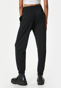 Zwarte joggpants met elastische tailleband en boorden, gemaakt van zachte stof. Kenmerken zijn zijzakken en een losse pasvorm. Combinatie met zwarte schoenen.