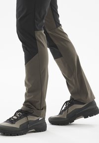 Wanderhosen in Schwarz und Olivgrün, mit tailliertem Design und kontrastierenden Einsätzen. Kombiniert mit schwarzem und grauem Wanderschuhen.