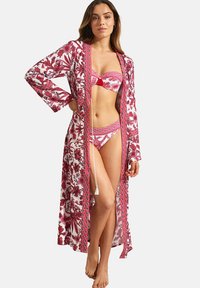 Lange bloemenjas in roze en wit. Heeft brede mouwen, een striksluiting met een kwastje, gedragen over een bijpassende bikini-set. Lichtgewicht stof.