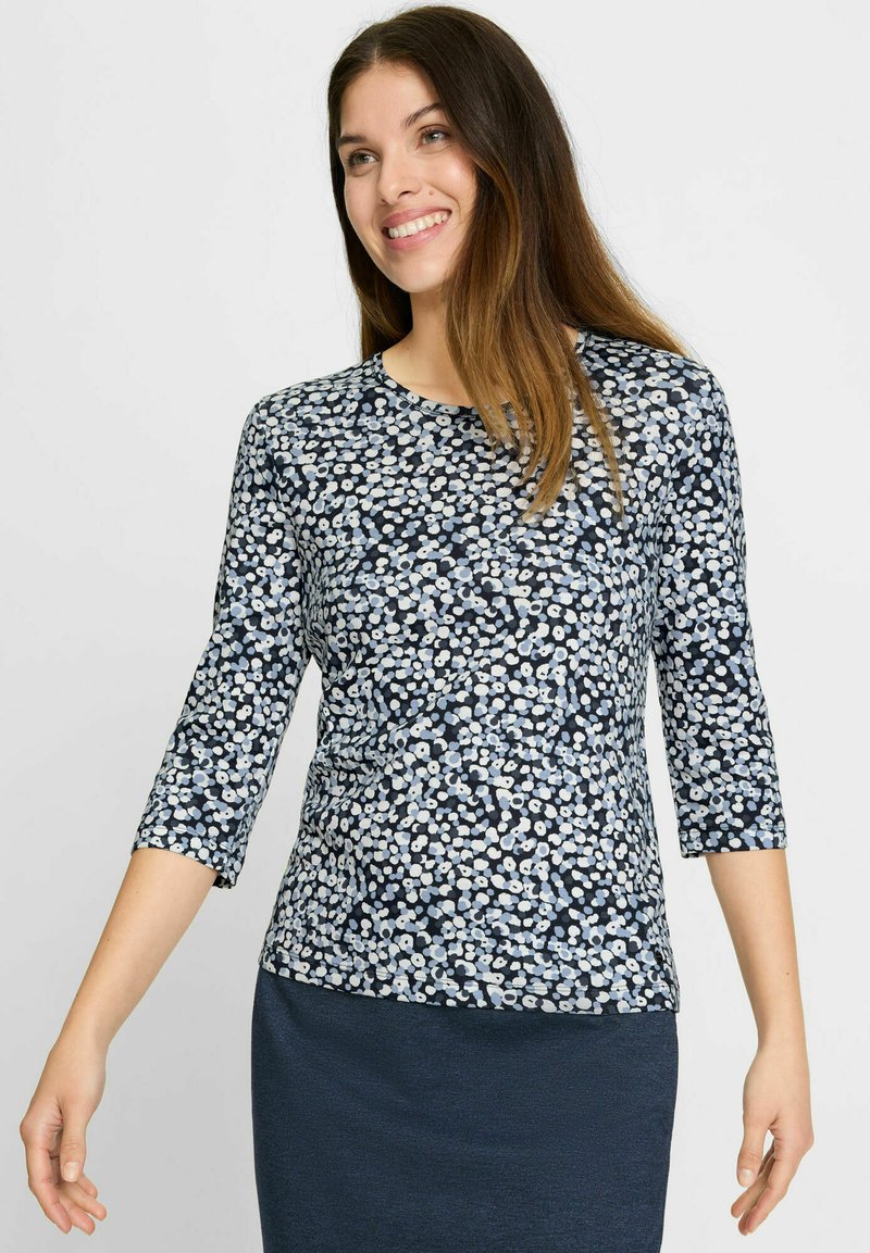 Bluse mit Blumenmuster und drei Viertelärmeln, auf einem marineblauen Hintergrund mit hellblauen Akzenten. Hergestellt aus weichem, leichtem Material.