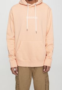 Felpa in cotone color pesca con tasca a marsupio, lacci e logo ricamato "PULL&BEAR". Presenta un taglio comodo e polsini a coste.