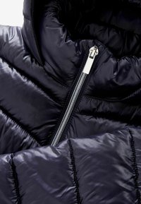 Doudoune bleu marine, avec un extérieur brillant matelassé, un col haut et une fermeture éclair argentée. Détails avec des panneaux horizontaux cousus.