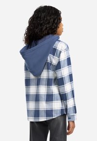 Καρό πουκάμισο με μπλε και λευκό καρό μοτίβο, με ναυτικό κουκούλα. Κατασκευασμένο από ύφασμα με λεία υφή, απεικονιζόμενο από πίσω.