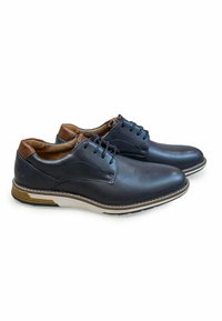 Zapatos de cuero azul marino con punta redondeada, acentos marrones y suela blanca y marrón en contraste. Presentan un diseño de cordones y detalles cosidos.