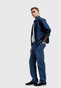 Chaqueta y pantalones de mezclilla en azul oscuro, combinados con una camisa blanca. Incluye dos bolsillos en la chaqueta y un corte relajado. Zapatillas negras.