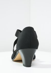 Scarpa nera con tacco, realizzata in tessuto strutturato, punta arrotondata e tacco a cono moderato. Presenta una fascia elastica attorno alla caviglia.