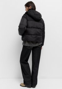 Giacca a vento nera con cappuccio, caratterizzata da un design trapuntato e cuciture visibili. Abbinate a jeans scuri e stivaletti beige.