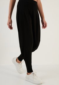 Zwarte, geplooide harempantalons van zachte stof, gecombineerd met witte sneakers. Kenmerkt een brede tailleband en een taps toelopend enkelontwerp.