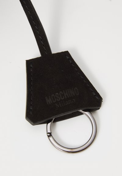 Must musta võtmehoidja, millel on tekstuuriga pind, metallring ja reljeefne "Moschino Milano" logo sildil.