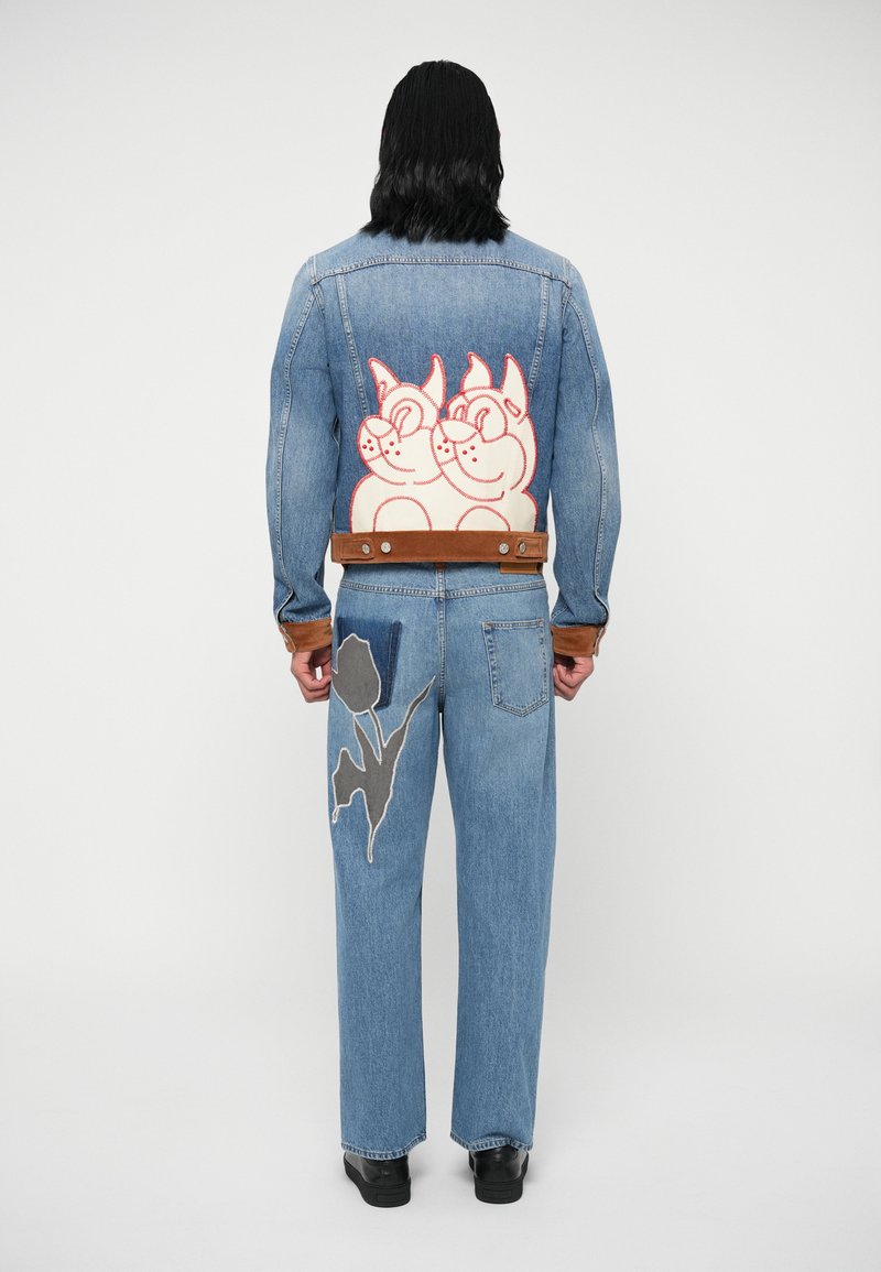 Τζάκετ τζιν με κέντημα ροζ και λευκής γάτας στο πίσω μέρος, συνδυασμένο με ανοιχτό μπλε τζιν που διαθέτει γκρι λουλούδι και καφέ λεπτομέρειες.