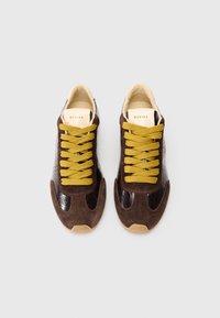 Brązowe zamszowe i błyszczące skórzane sneakersy z żółtymi sznurowadłami, zaokrąglonym noskiem i teksturowanymi akcentami. Posiadają subtelną grafikę na języku.