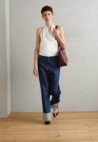 Top bianco senza maniche, jeans larghi blu scuro con orli risvolti, borsa borgogna e tacchi rossi a punta, su uno sfondo neutro.