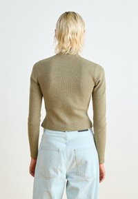 Oliwkowy sweter z prążkowanej dzianiny z długimi rękawami, dopasowaną sylwetką i wysokim kołnierzem. Połączony z jasnoniebieskimi dżinsami o wysokim stanie.