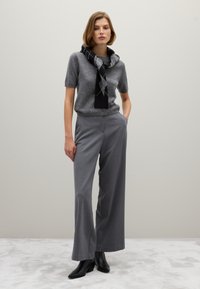 Top de punto gris de manga corta con una bufanda de patrones en blanco y negro, combinado con pantalones grises de pierna ancha y botas de tobillo negras sobre un fondo claro.