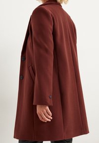 Viininpunainen villasekoitepäällystakki, jossa on räätälöity leikkaus, lovellinen kaulus, sivutaskut ja mustat napit hihoissa.