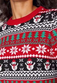 Pull en tricot avec un col côtelé rouge, présentant un fond noir et des motifs de bonhommes de neige, d'arbres et de flocons de neige en vert et blanc.