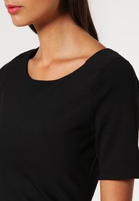 Mustat lyhythihaiset paidat, joissa on sileä kangas, laaja pyöreä kaula-aukko ja sovitettu siluetti. Ei näkyviä kuvioita tai koristeita.