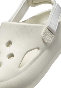 Białe plastikowe klapki z otworami wentylacyjnymi, teksturowaną powierzchnią i białym regulowanym paskiem z wzorzystym akcentem.