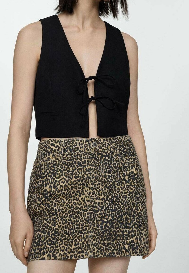Schwarzes Crop-Top mit tiefem V-Ausschnitt und vorderem Bindedetail, kombiniert mit einem beigen Rock mit schwarzem Leopardenmuster.