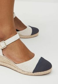 Beige és tengerészkék vászon felsőrészű espadrill szandál, kerek orral, csatos bokapánttal és fonott juta középtalppal.