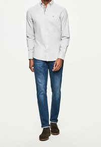 Camicia grigia chiaro con maniche lunghe e collo a quadri, abbinata a jeans blu e scarpe in camoscio marroni.