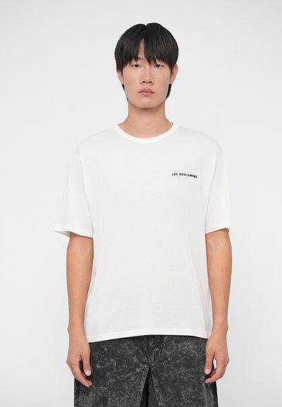 Camiseta de algodón blanca con manga corta y cuello redondo. Presenta una pequeña impresión negra con "LES BENJAMINS" en el lado izquierdo del pecho.