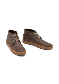 Bottines en cuir marron avec une texture lisse, semelle en caoutchouc marron contrastante et design traditionnel à lacets. Coutures subtiles visibles.