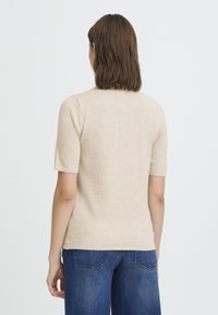 Haut beige ajusté à manches courtes avec un col rond. Le tissu semble doux et léger, associé à un jean large bleu foncé.