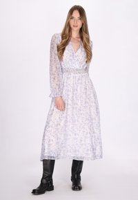 Helles lila Blumenkleid mit langen Ärmeln, das Rüschenmanschetten und eine geraffte Taille aufweist, kombiniert mit knielangen schwarzen Stiefeln.