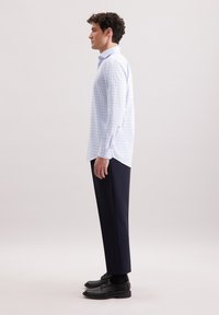 Camicia a quadri azzurro chiaro realizzata in tessuto intrecciato, abbinata a pantaloni blu scuro e scarpe nere. La camicia presenta un colletto con bottoni e polsini.