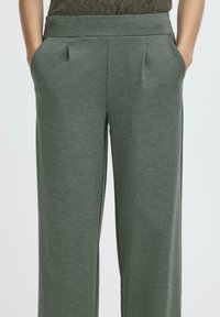 Pantaloni largi verzi, cu textură, cu un talie plată, având buzunare laterale și plissaje subtile pentru un aspect elegat.