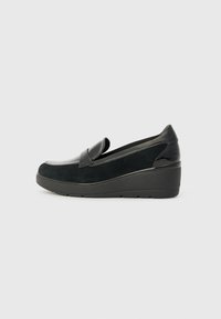 Chaussure slip-on en Suède noire avec un accent en cuir verni noir brillant, semelle compensée et un design de bout arrondi et lisse.