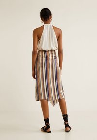 Haut dos-nu en tissu blanc associé à une jupe rayée longueur genou avec des nuances de beige, violet et orange, et des sandales noires à brides.