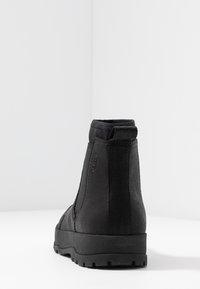 Černé kotníkové boty s hladkým povrchem, elastickými postranními panely, poutkem na zadní straně a robustní podešví pro lepší trakci.