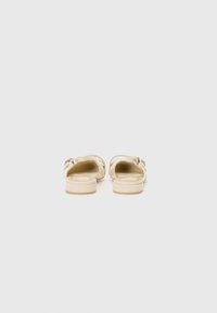 Sandales à enfiler beiges avec une finition brillante, présentant une sangle de largeur moyenne et un petit talon arrondi. Les accents incluent un détail de boucle simple.
