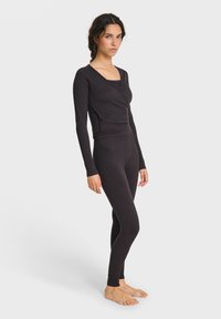 Dunkelgraues, eng anliegendes Langarmoberteil mit Wickeldesign, kombiniert mit passenden Leggings. Hergestellt aus weichem, dehnbarem Material.