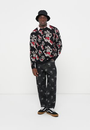 Zwarte gebreide trui met rode en witte grafische ontwerpen, gecombineerd met zwarte broek met witte yin-yang patronen, afgewerkt met zwart-witte sneakers.