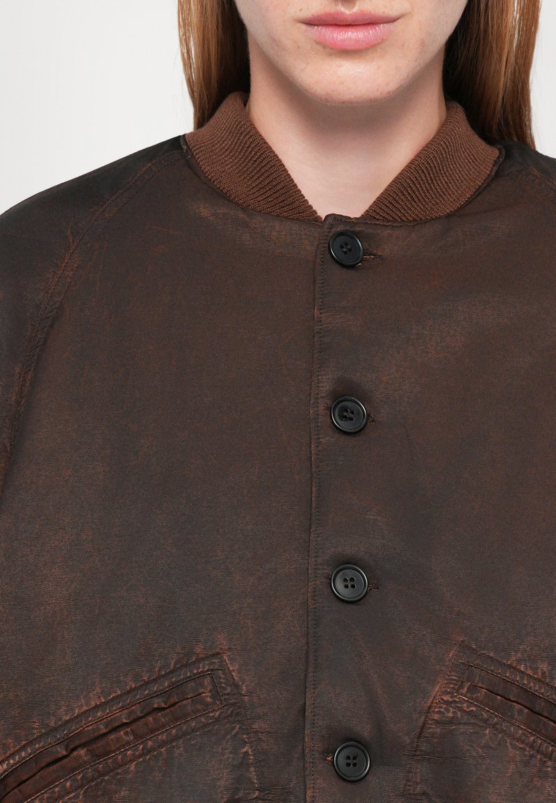 Veste marron à boutonnière avec un col côtelé, dotée d'un tissu texturé et de deux poches angulaires. Six boutons noirs le long de l'avant.