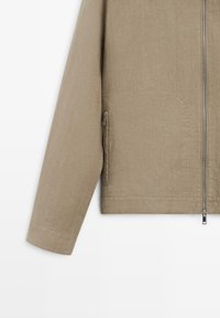 Beige langærmet jakke med lynlås foran og lynlåslomme i siden, med enkel manchet og tekstureret stof.