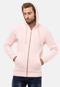 Lichtroze zip-up hoodie met een voorzijde ritssluiting, verstelbare trekkoordcapuchon en zijzakken. Beschikt over ribgebreide manchetten en een zoom. Soepele textuur.