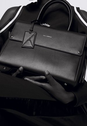 Sac à main en cuir noir avec un design structuré, une texture lisse, des poignées supérieures et un petit logo de marque embossé à l'avant.